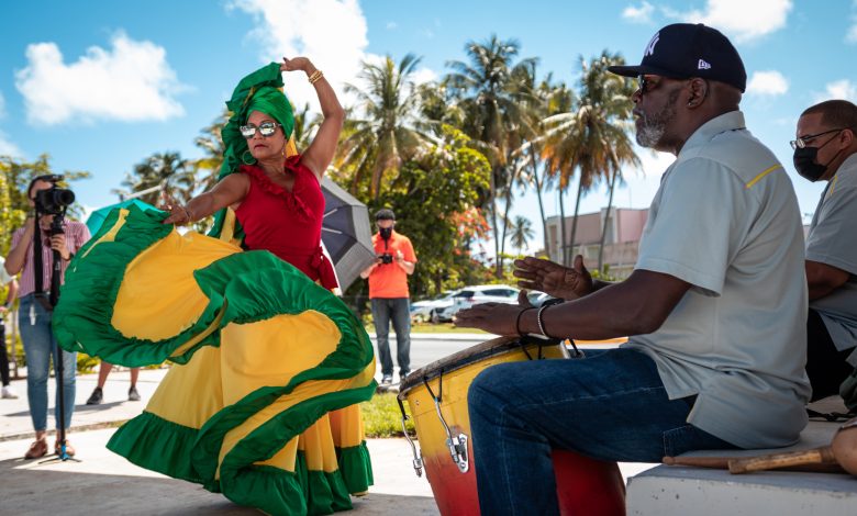 Mujer bailando bomba en Loíza con flda de color verde y amarilla y una camisa roja, los colores de la bandera. Mientras tanto, dos hombres tocan los tambores.